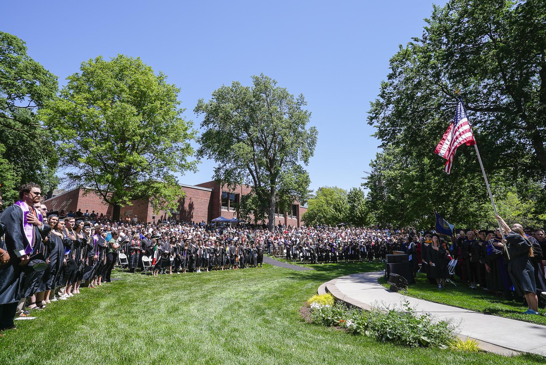 People fill the steps of an outdoor amphitheater, turned toward an American flag with their h和s over their hearts.