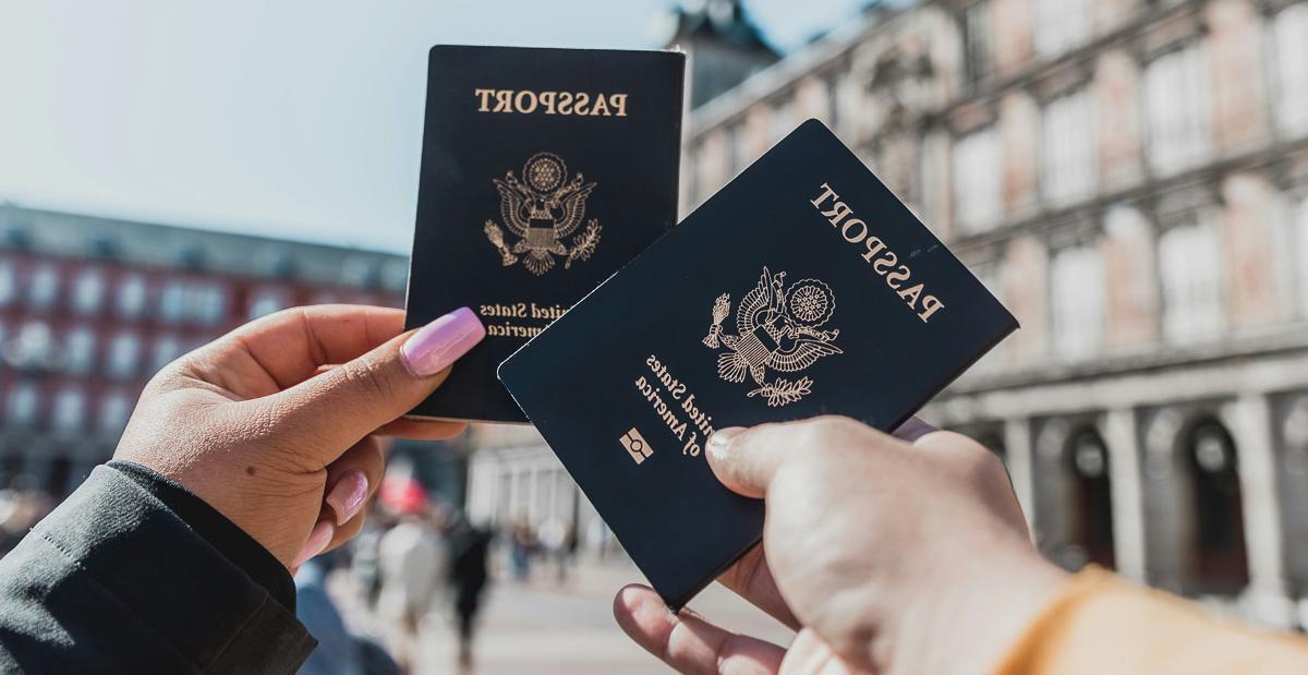 Image by Spencer Davis, through Unsplash. Two people hold up blue U.S. passports in front of an unidentified building. The image shows only their hands and they're holding the passports together in a "cheers" gesture.